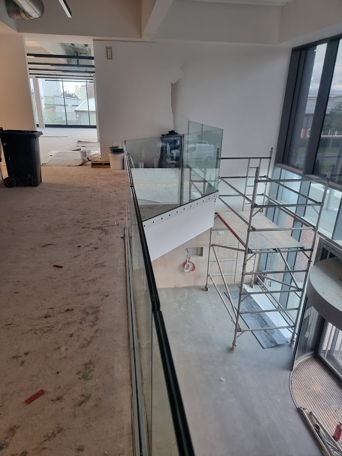 Frameless glass mezzanine in a double-height office lobby — further view of the completed installation