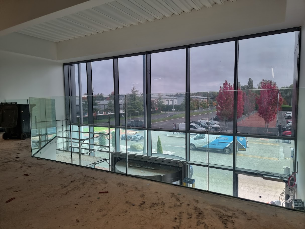 Frameless glass mezzanine in a double-height office lobby — further view of the completed installation