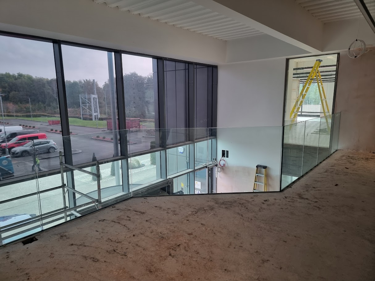 Frameless glass mezzanine in a double-height office lobby — further view of the completed installation